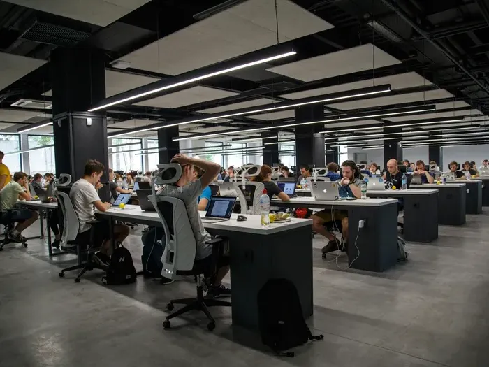 Large modern open-plan office with employees working on laptops at shared desks under bright lighting for Town Service Now